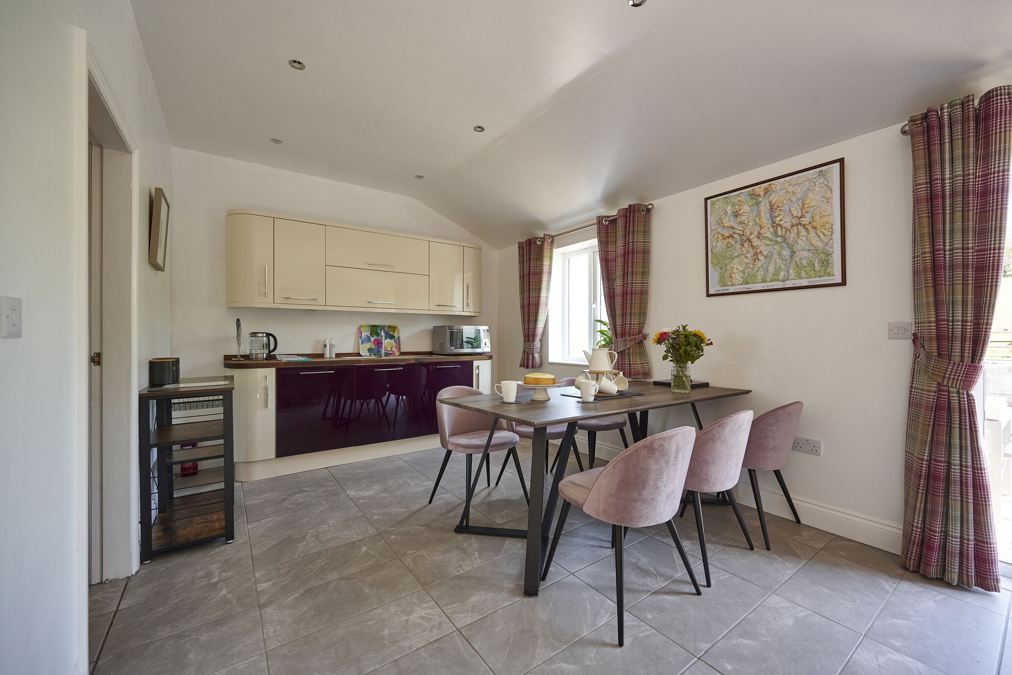 A modern kitchen with dark cabinets, a dining table with chairs, and a window with curtains.