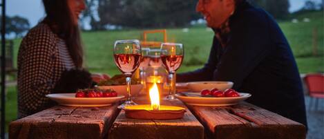 Een houten picknicktafel met borden vol eten en glazen wijn, buiten opgesteld met een kaars in het midden.