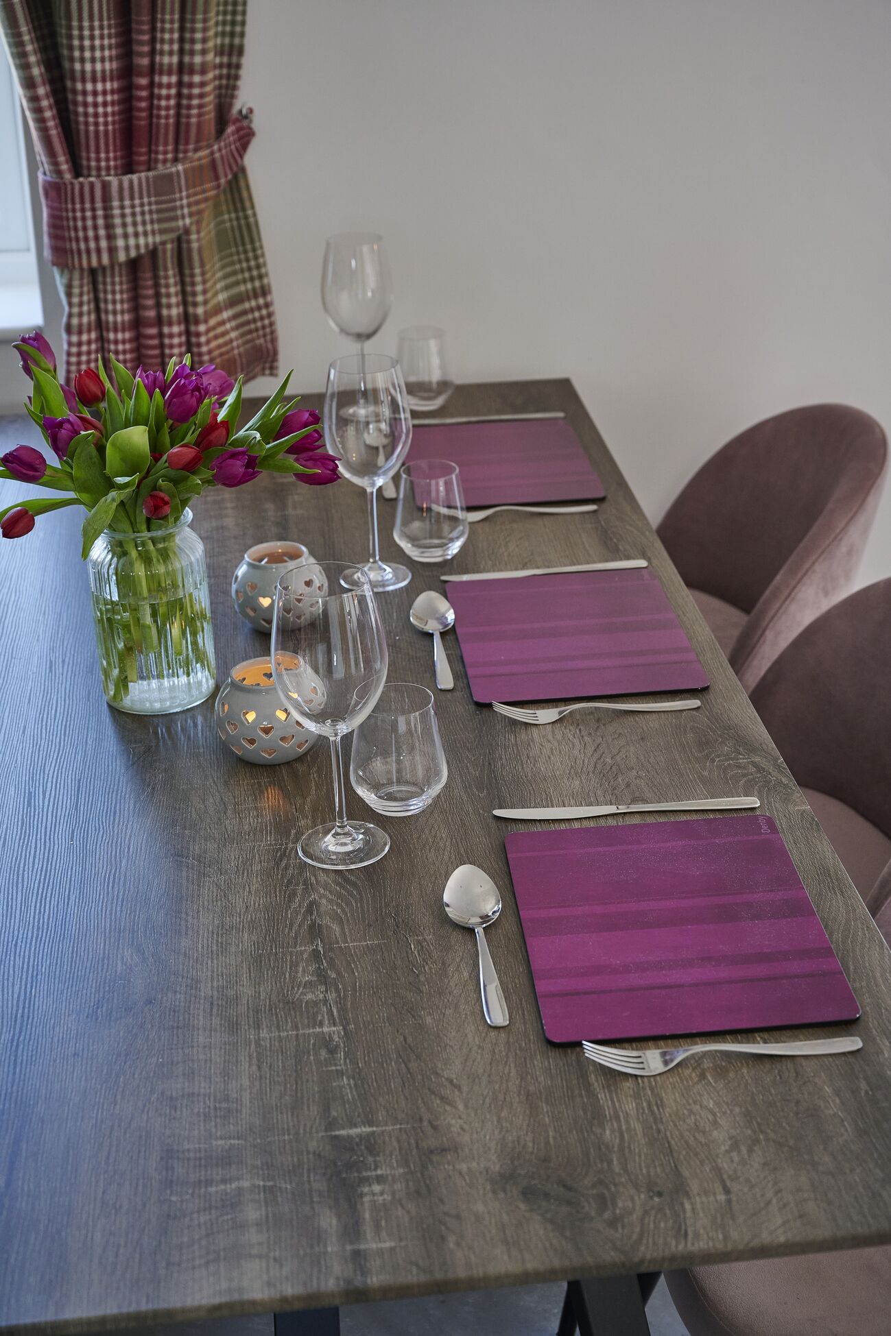 A dining table set with purple napkins, clear wine glasses, and a vase of purple and red tulips.