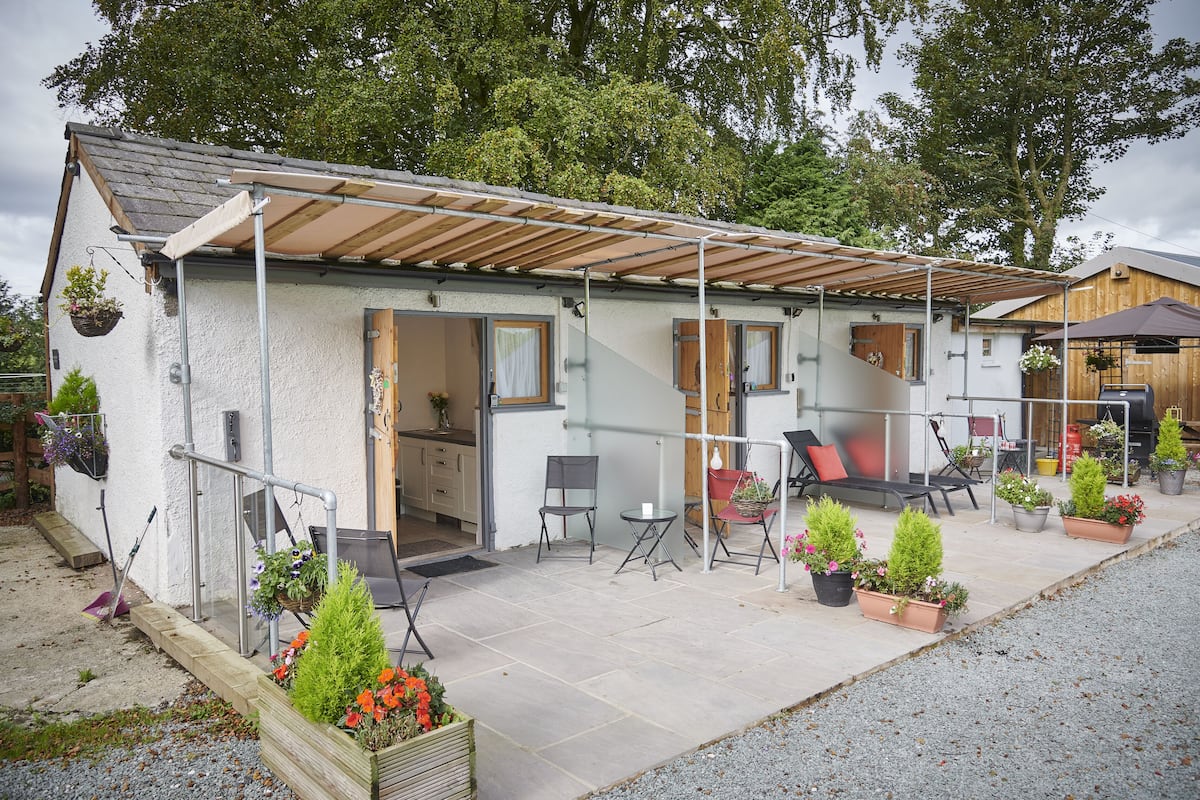 A small, single-story house with a covered patio area, outdoor seating, and potted plants.
