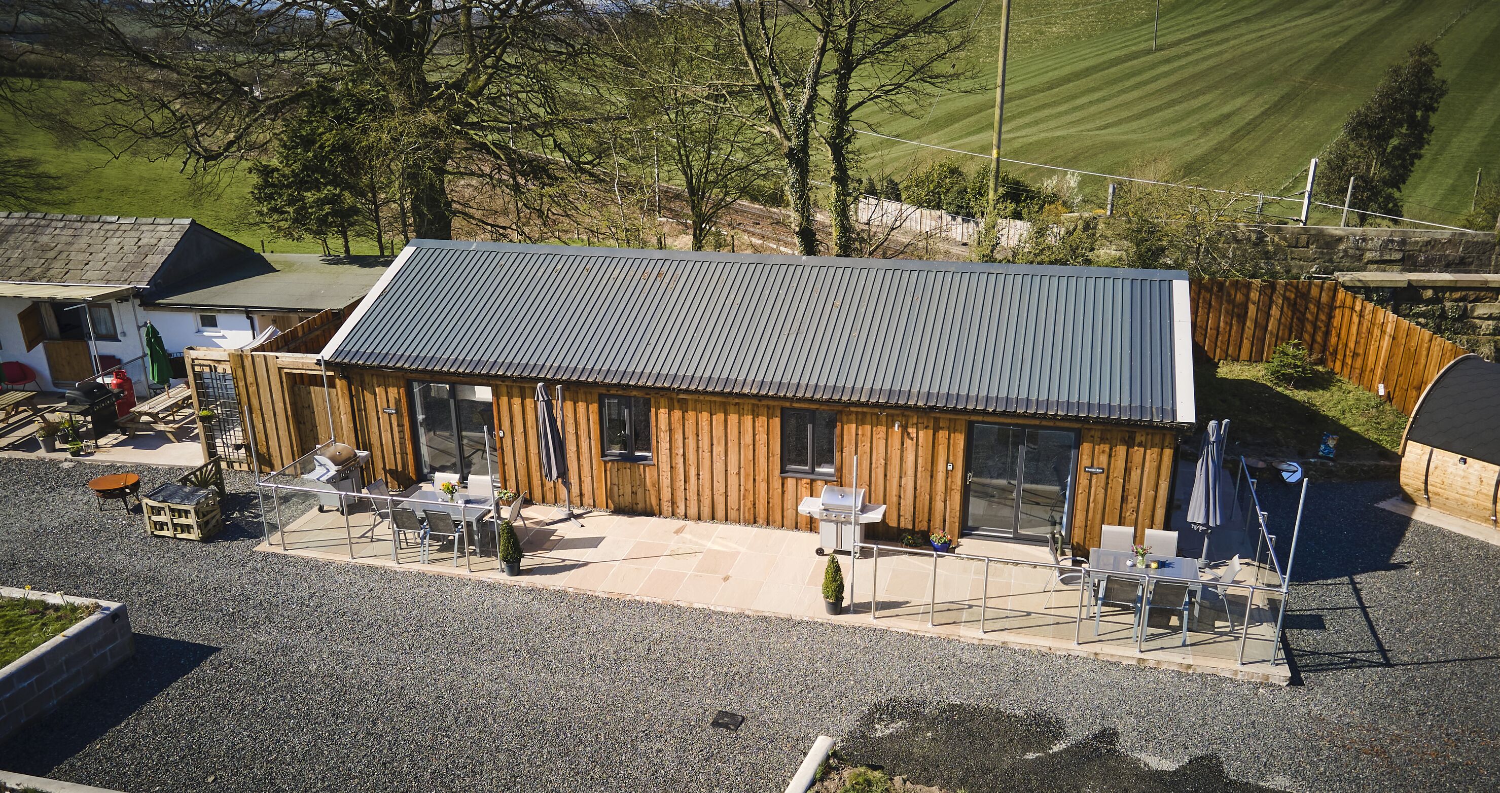 A wooden building with a metal roof, outdoor seating, and a gravel driveway.