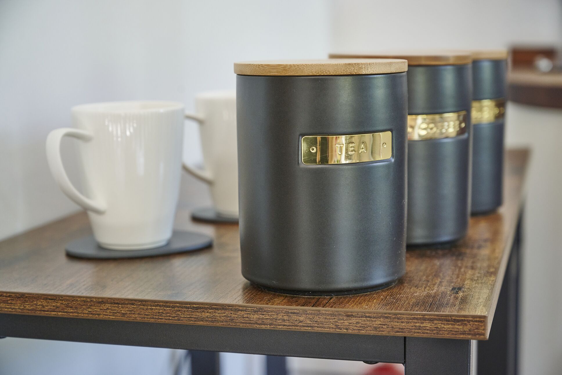 Une rangée de tasses noires ornées de motifs dorés, posées sur une table en bois.