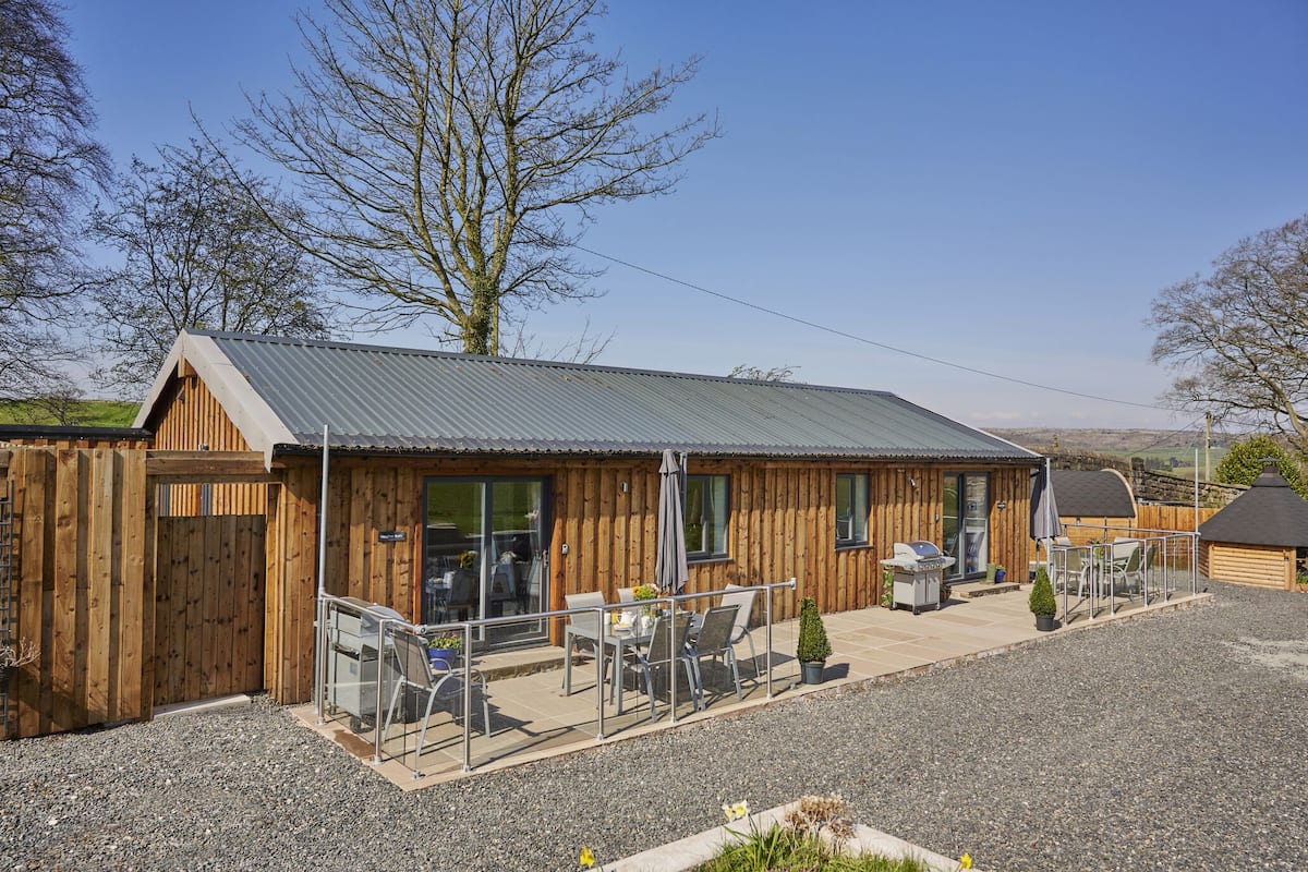 A wooden building with a metal roof, a patio with tables and chairs, and a barbecue area.