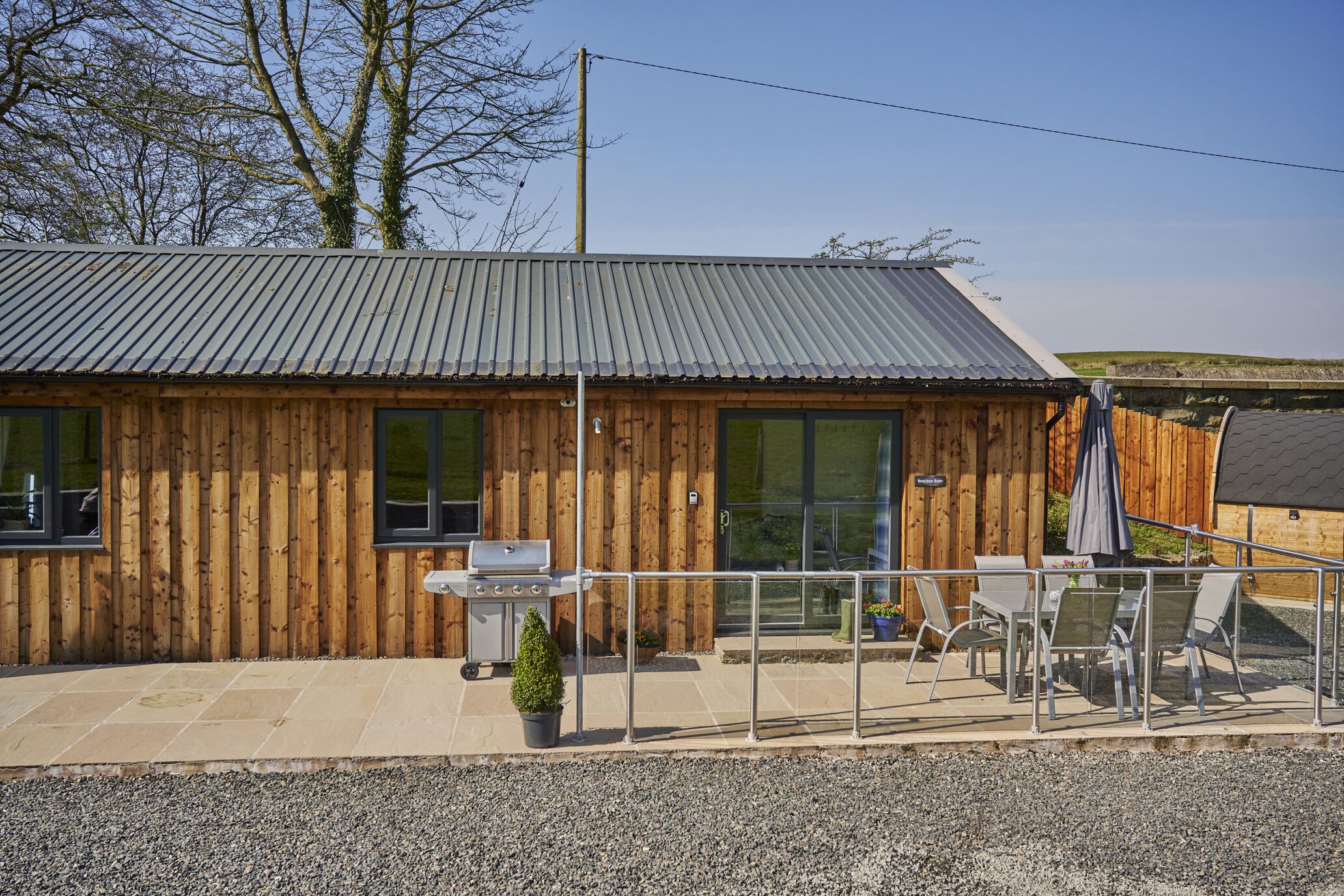 A wooden building with a metal roof, a barbecue grill, and outdoor seating with a table and chairs.