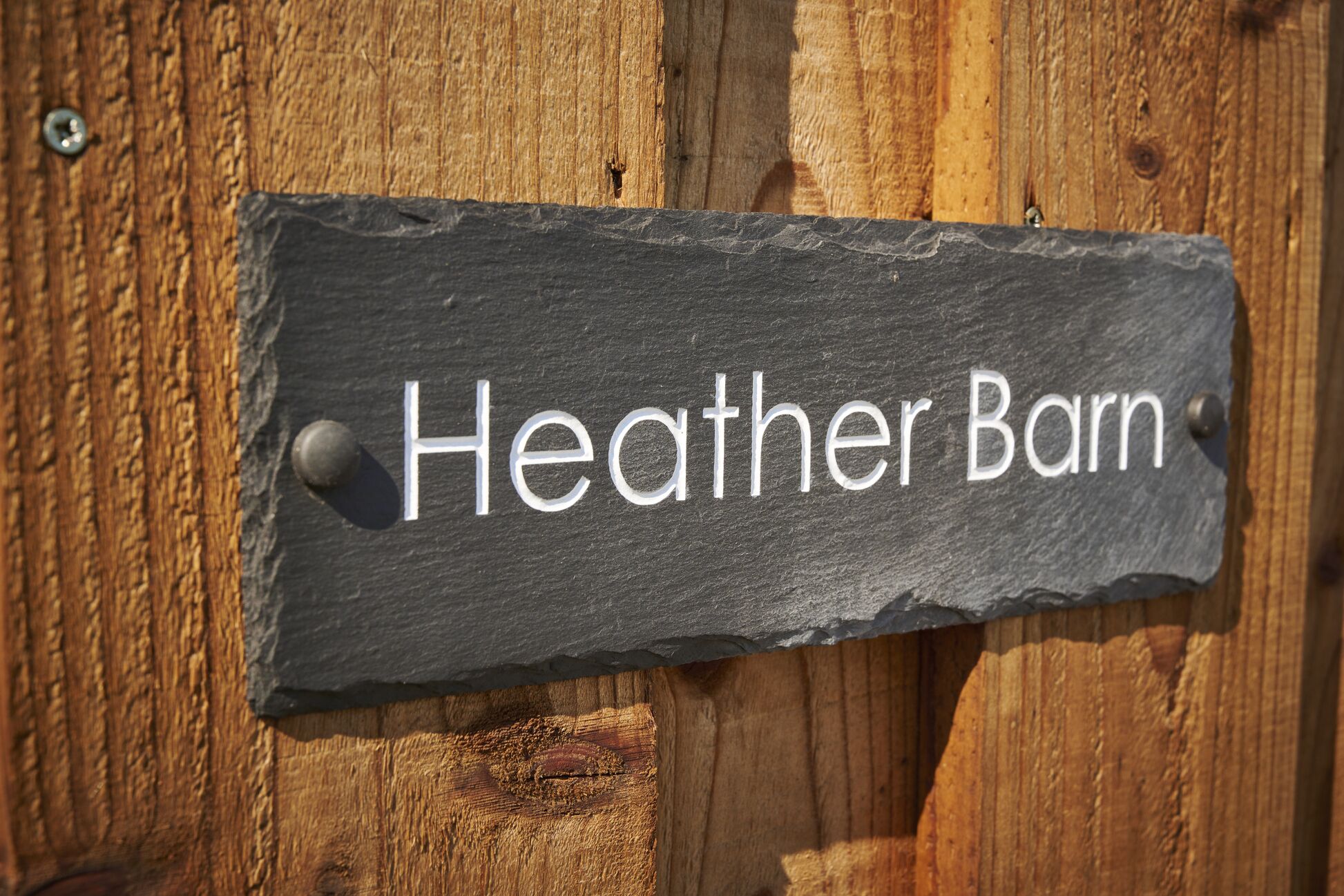 A slate sign with the text "Heather Barn" mounted on a wooden surface.