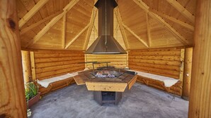 A wooden cabin with a central wood-burning stove, benches, and a high ceiling with wooden beams. - Newlands Farm Stables (Kendal)