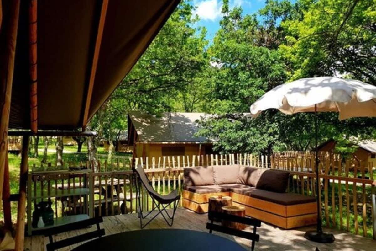 Une terrasse extérieure avec une table en bois, un coin salon confortable et un grand parasol.