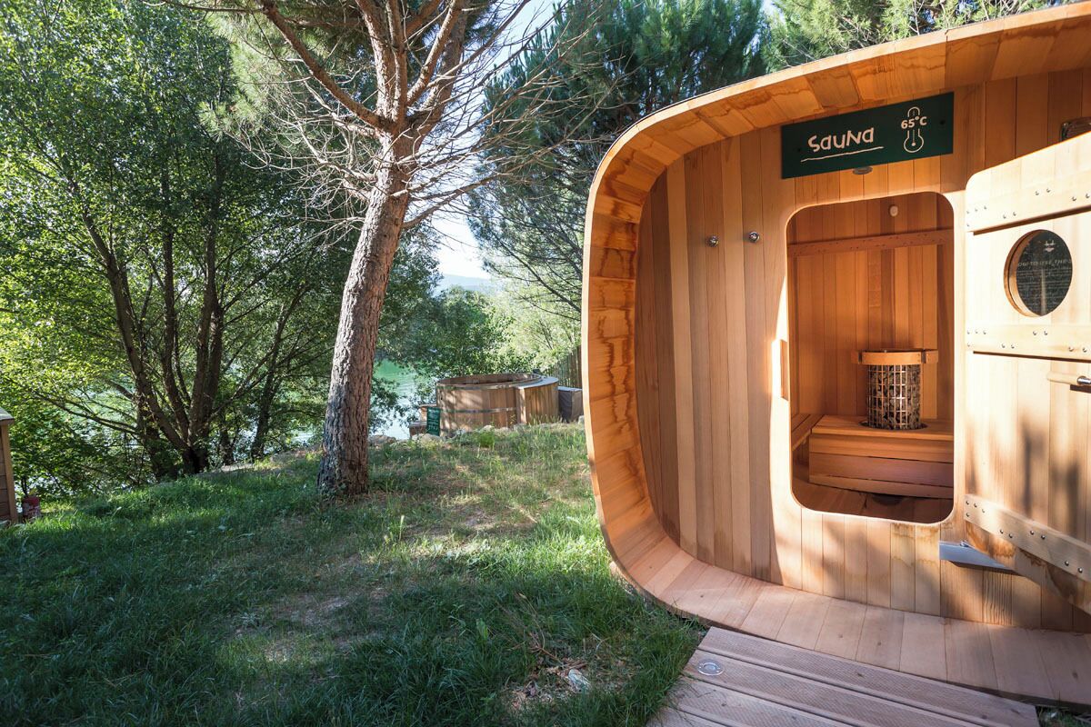 Eine Holzsauna mit einem Schild, das 65°C anzeigt, umgeben von Bäumen und einer Wiese.