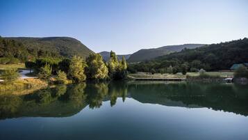 Un lago tranquilo con reflejos de árboles y colinas, rodeado de vegetación y algunos edificios.