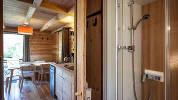 A wooden cabin interior with a kitchen area, dining table, and a shower.