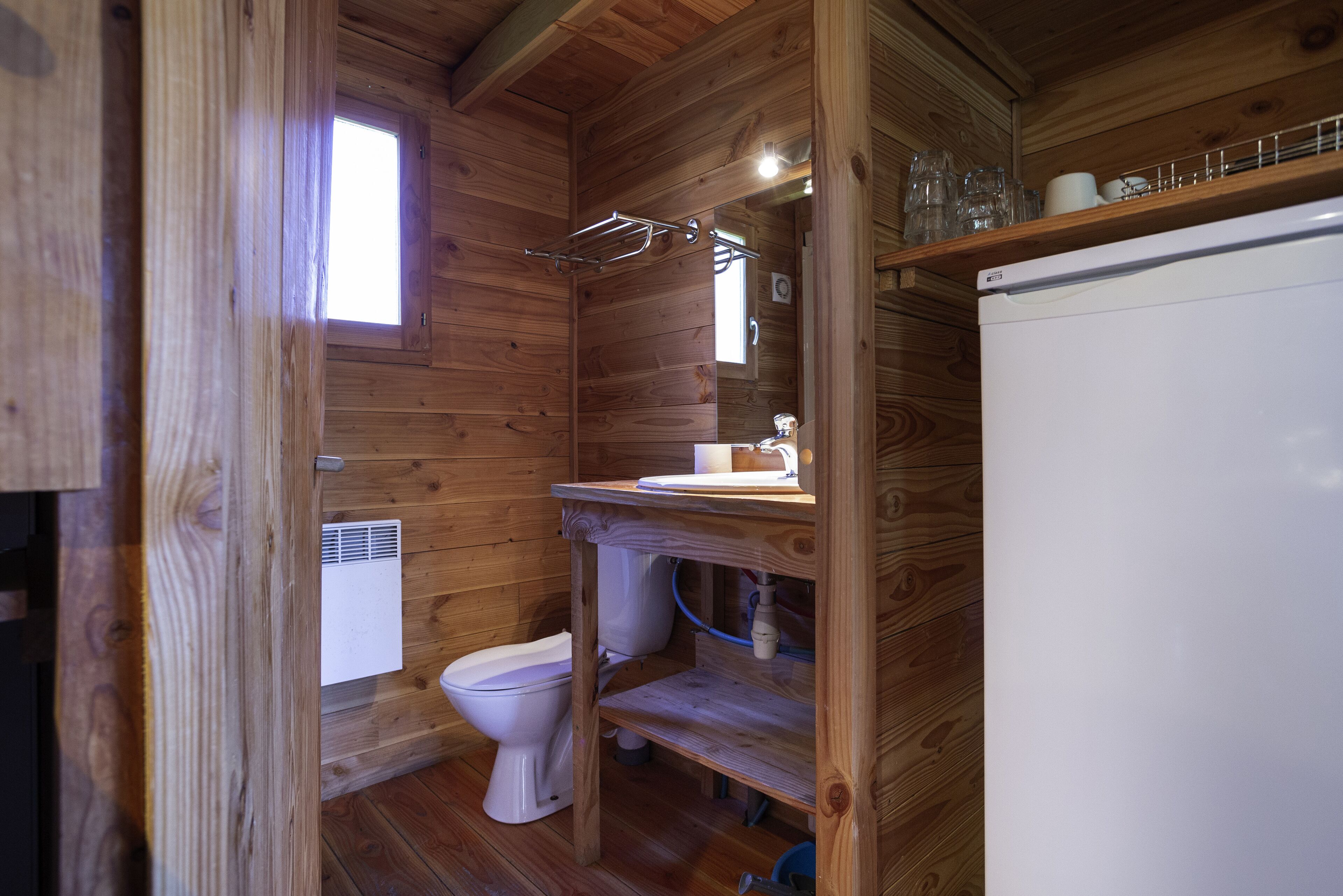 A compact wooden cabin bathroom with a toilet, sink, and a small window.