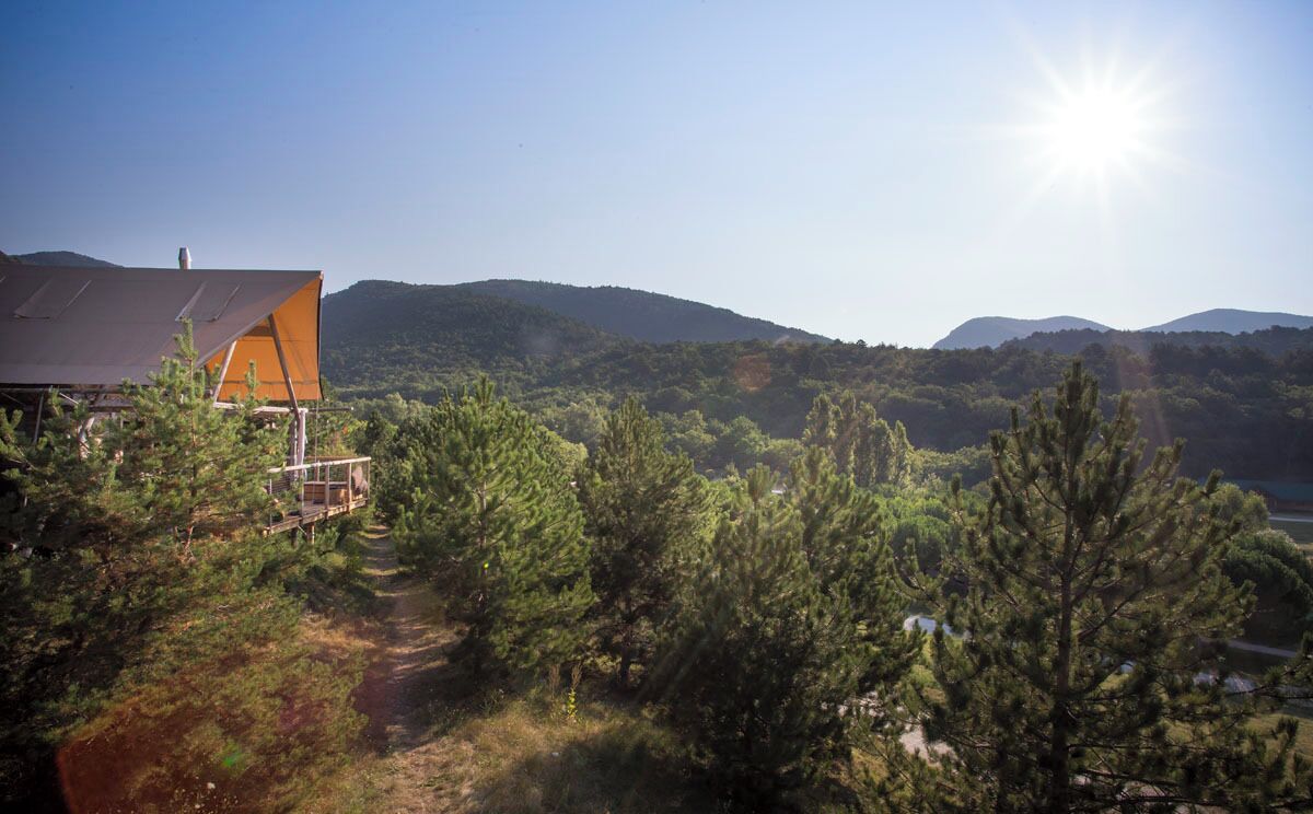 Una casa con techo inclinado y terraza de madera, rodeada de densos pinos y colinas al fondo.