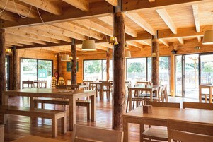 Interior de madera con mesas, bancos, ventanas amplias y lámparas colgantes.