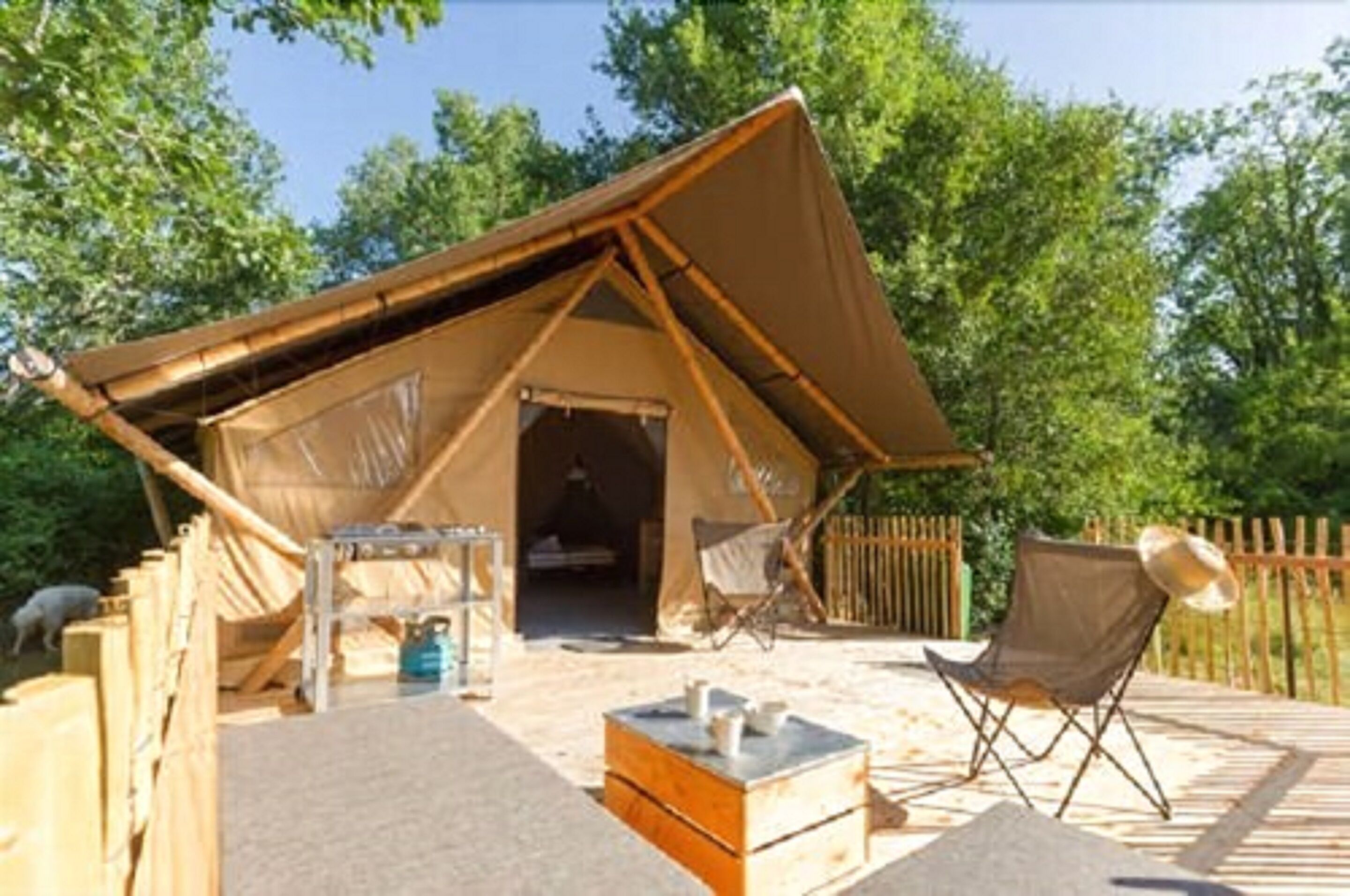 Un hébergement sous tente doté d’une terrasse en bois, d’une petite table et de deux chaises.