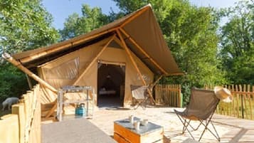 Un hébergement sous tente doté d’une terrasse en bois, d’une petite table et de deux chaises.