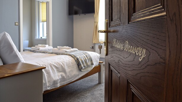 A hotel room with a bed, a television mounted on the wall, and a wooden door with a keyhole.