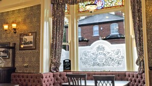 A room with a bay window, a chandelier, a patterned wall, and a view of a building outside.