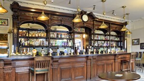 A bar with wooden decor, multiple shelves of bottles, and hanging lights.