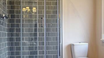 Ein modernes Badezimmer mit Duschkabine aus Glas, einer weißen Toilette und einem beige gefliesten Boden.