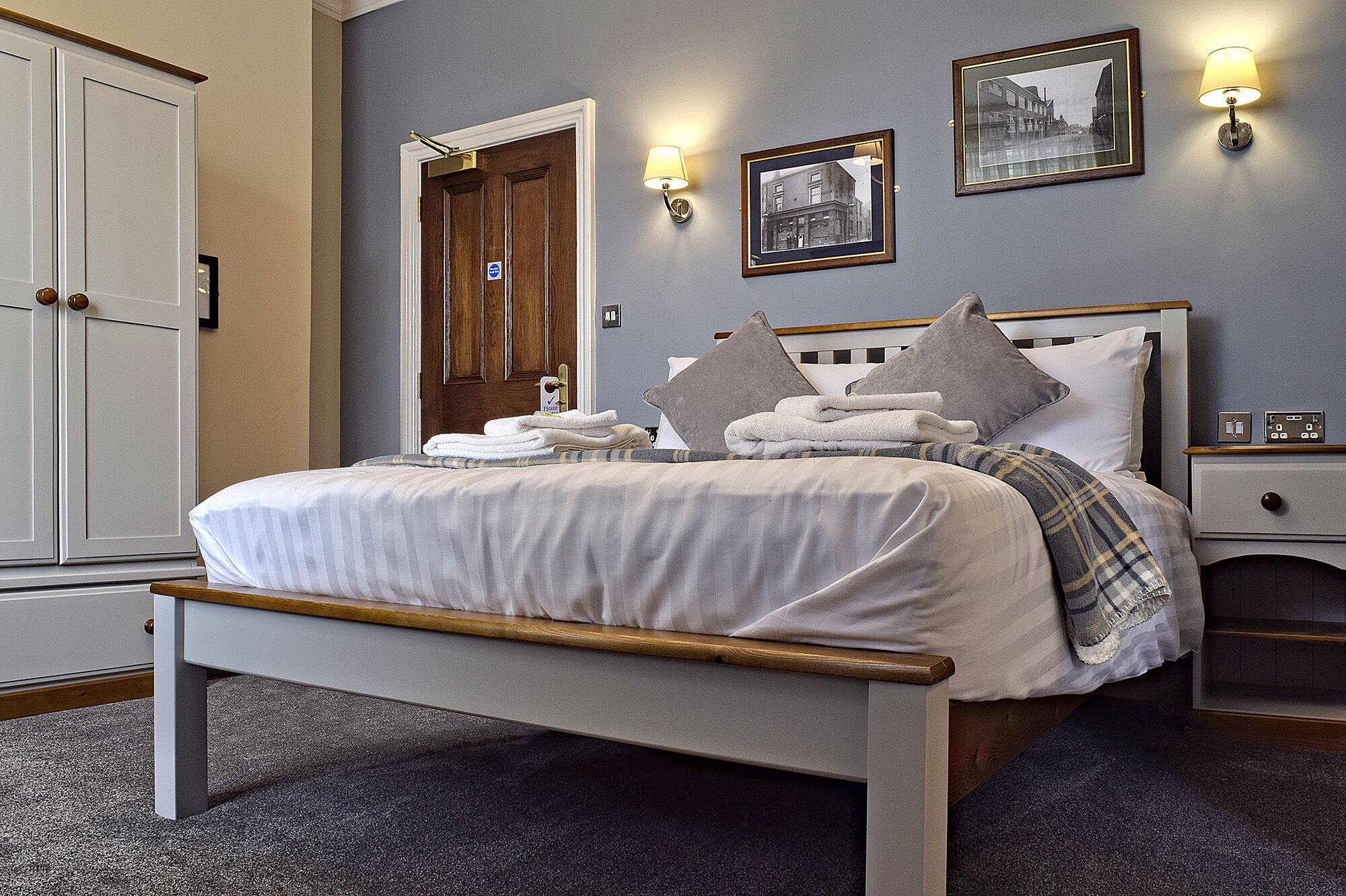 A neatly made bed with pillows and folded towels, a bedside table with a lamp, and a framed picture on the wall.