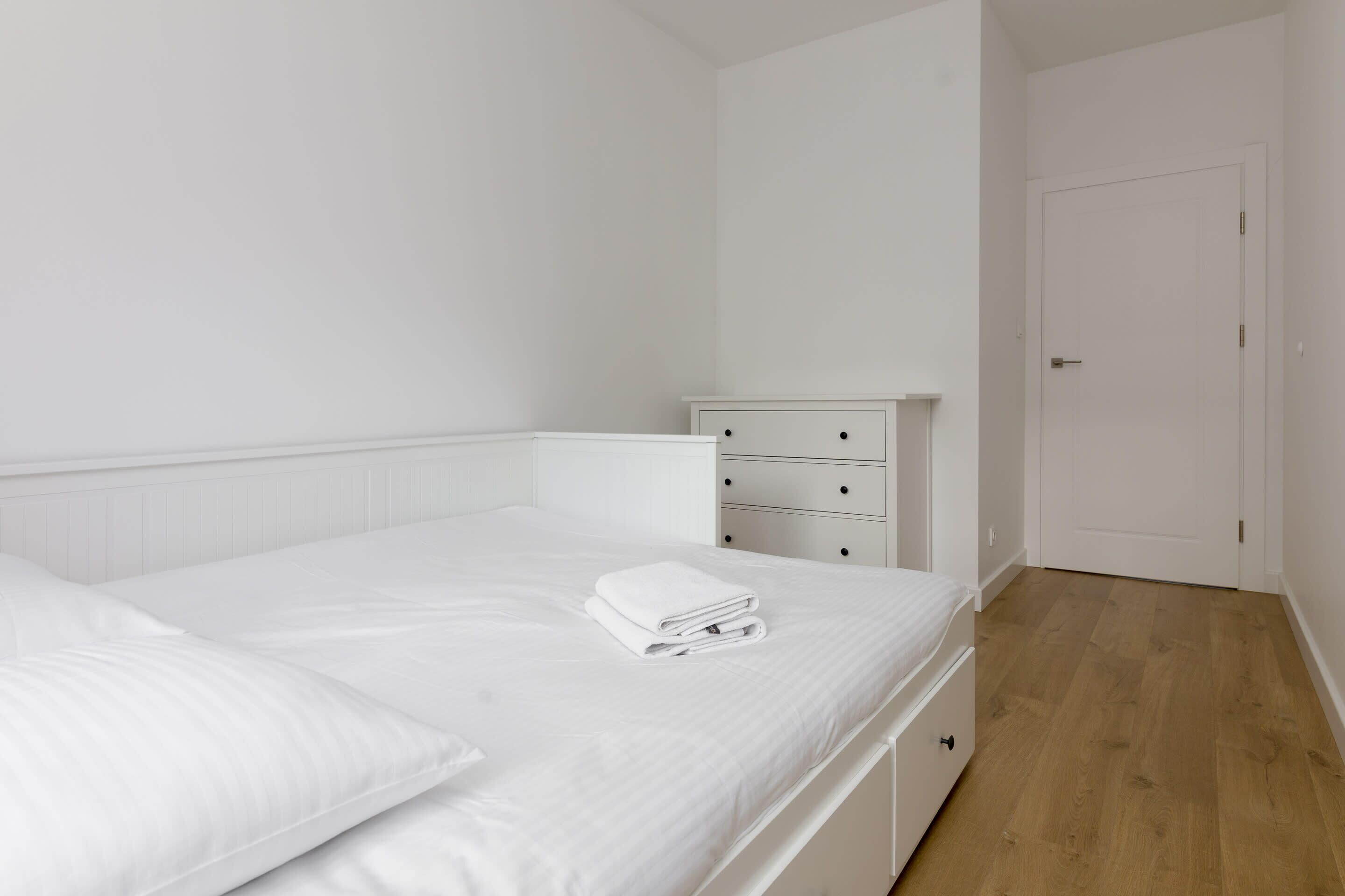 A bedroom with a bed, a nightstand, a dresser, and a door.