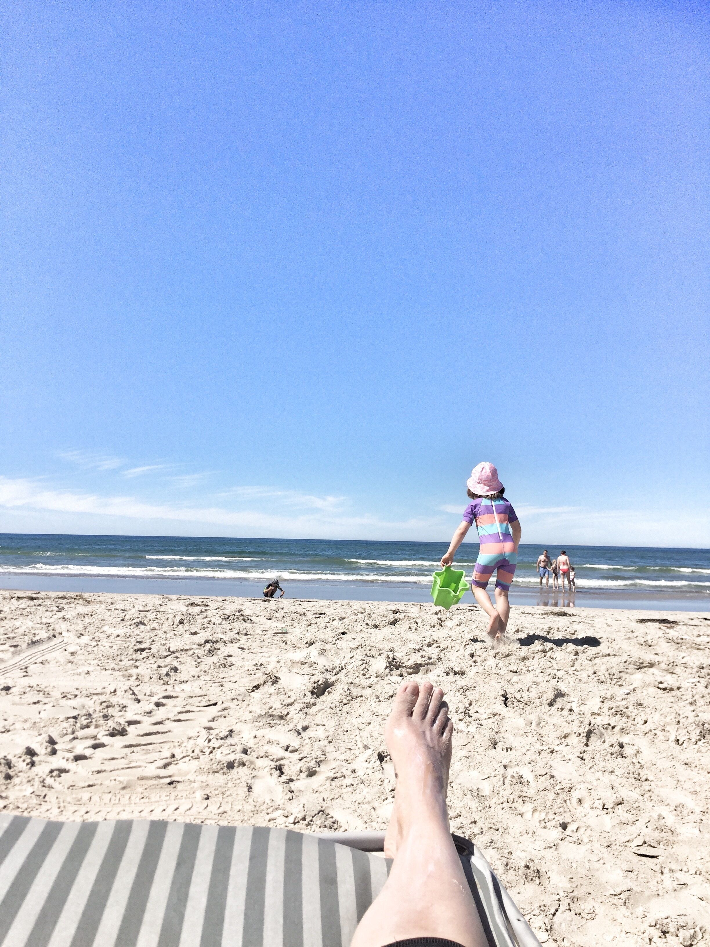 Escena de playa con una persona recostada en una silla de baño a rayas, mirando al océano.