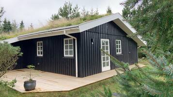 A black wooden cabin with a sloped roof, white trim, and a small porch area with a potted plant.