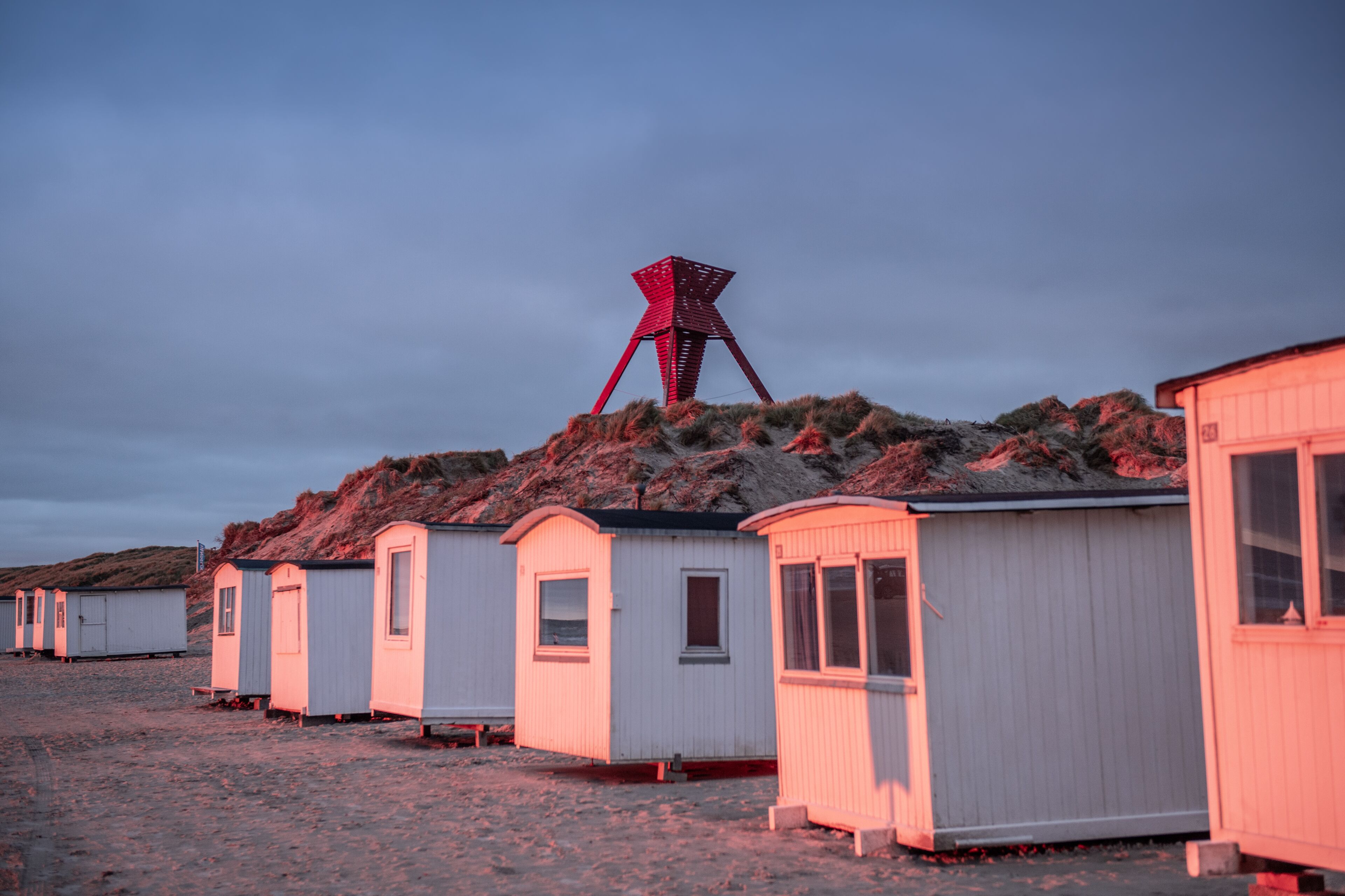 Une rangée de petites maisons mobiles blanches, avec un moulin à vent rouge en arrière-plan.
