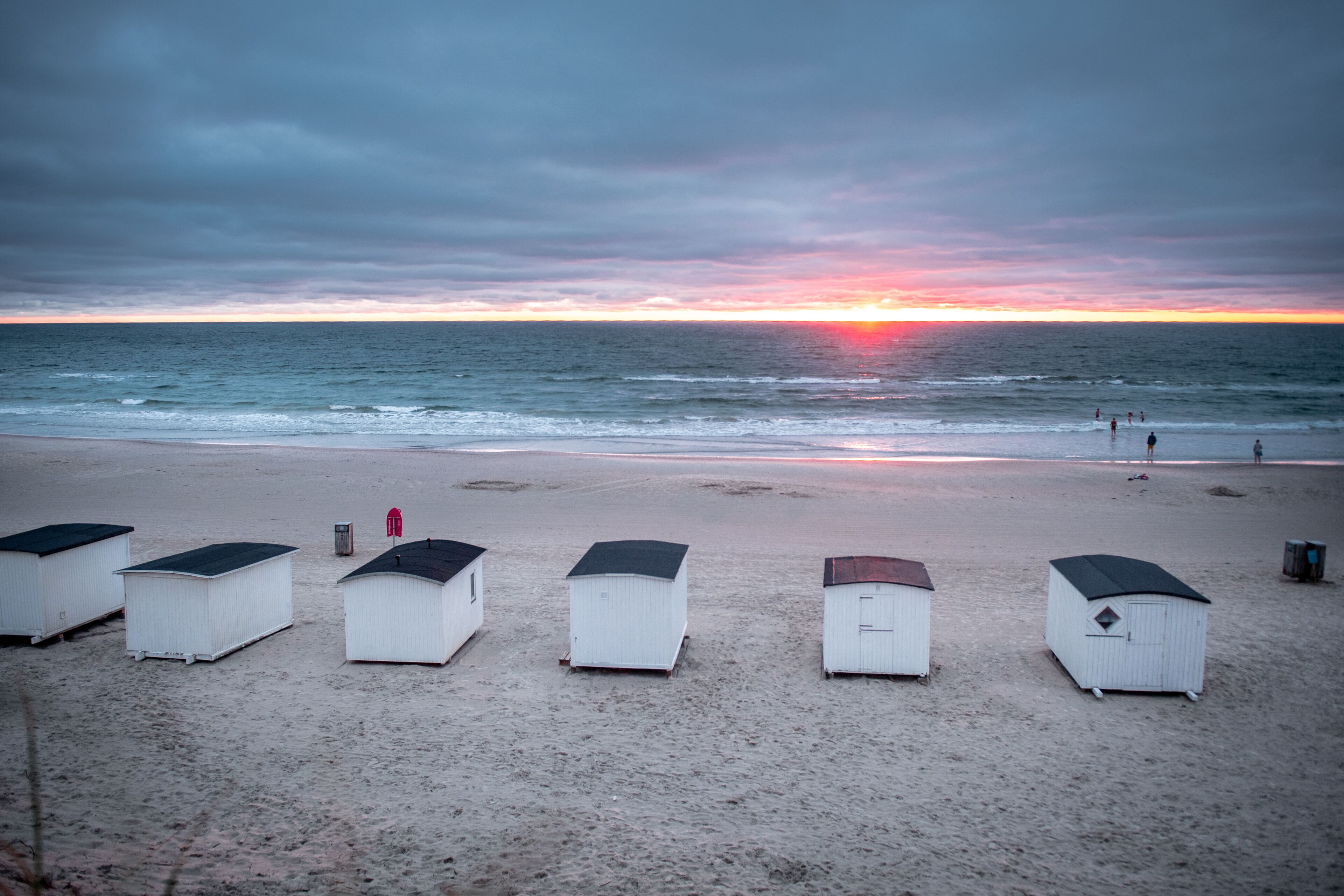 Beach huts aligned on the shore with the ocean in the background.