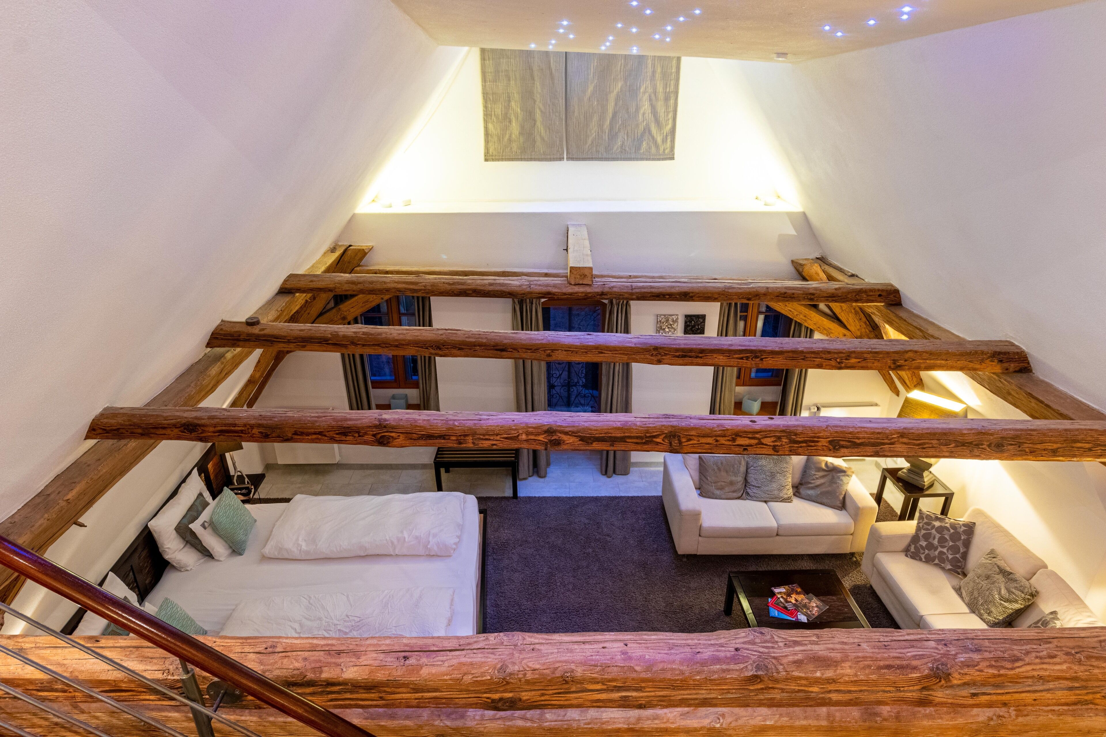 A loft-style bedroom with a wooden ceiling, a bed, a sofa, and a small table.