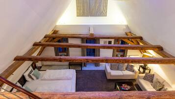 A loft-style bedroom with a wooden ceiling, a bed, a sofa, and a small table.
