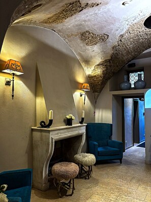 A room with a fireplace, two wall-mounted lamps, a blue armchair, and a small stool. - Hotel Herrnschloesschen (Rothenburg ob der Tauber)