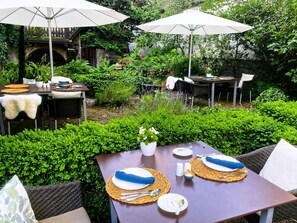 An outdoor patio with tables set for dining, surrounded by lush greenery and a stone archway. - Hotel Herrnschloesschen (Rothenburg ob der Tauber)