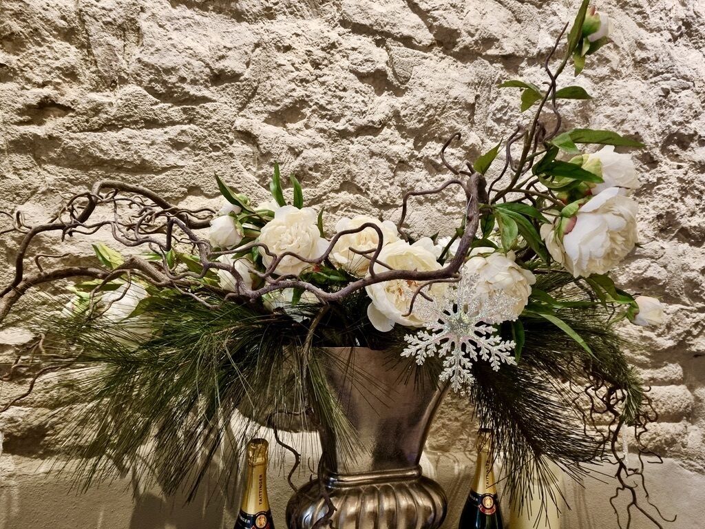 A decorative vase with white flowers and pine branches against a textured wall.
