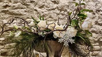 A decorative vase with white flowers and pine branches against a textured wall.