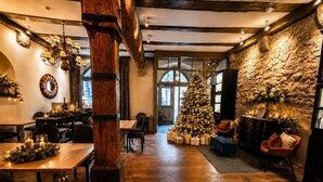 A cozy dining area with wooden tables, a large Christmas tree, and a stone wall with carvings. - Hotel Herrnschloesschen (Rothenburg ob der Tauber)