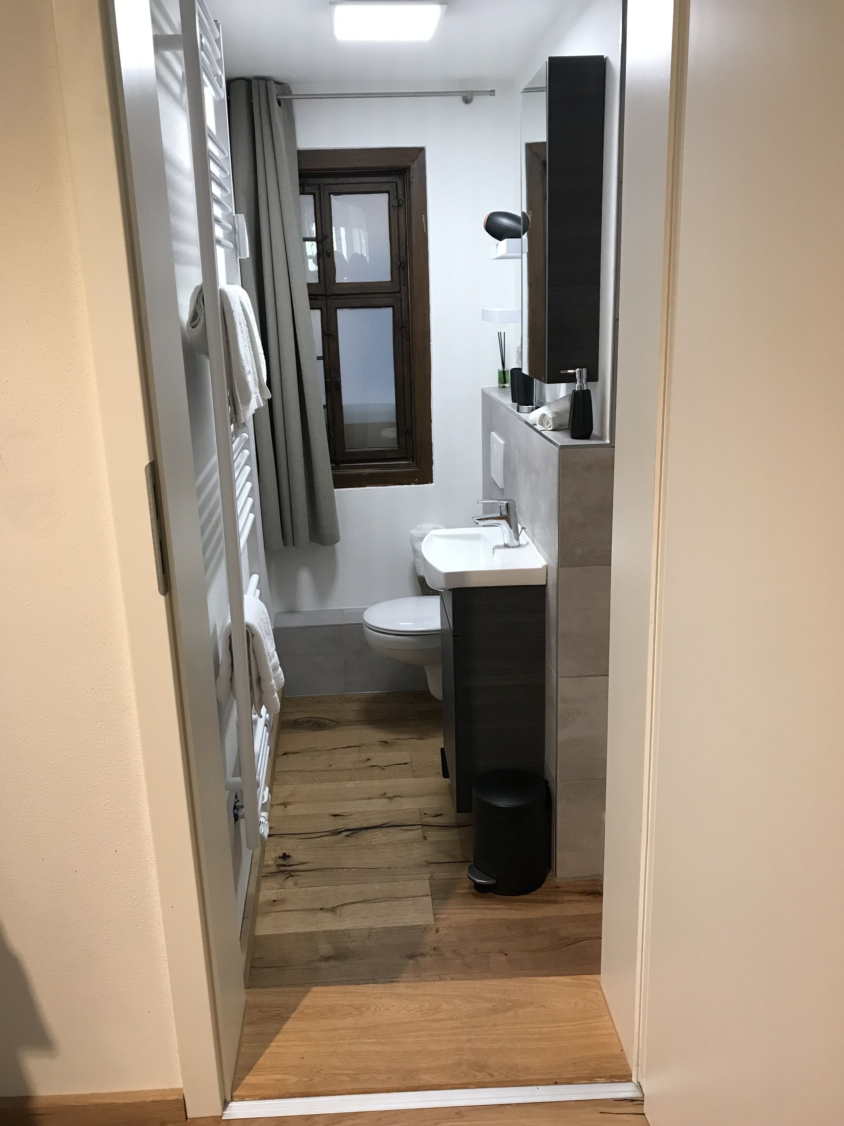 Un pasillo estrecho que conduce a un baño con inodoro, lavabo y toallero.