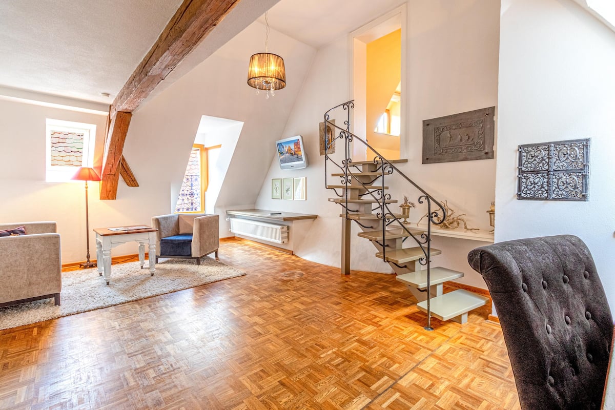 A spacious loft with a wooden floor, a modern staircase, and a cozy seating area.