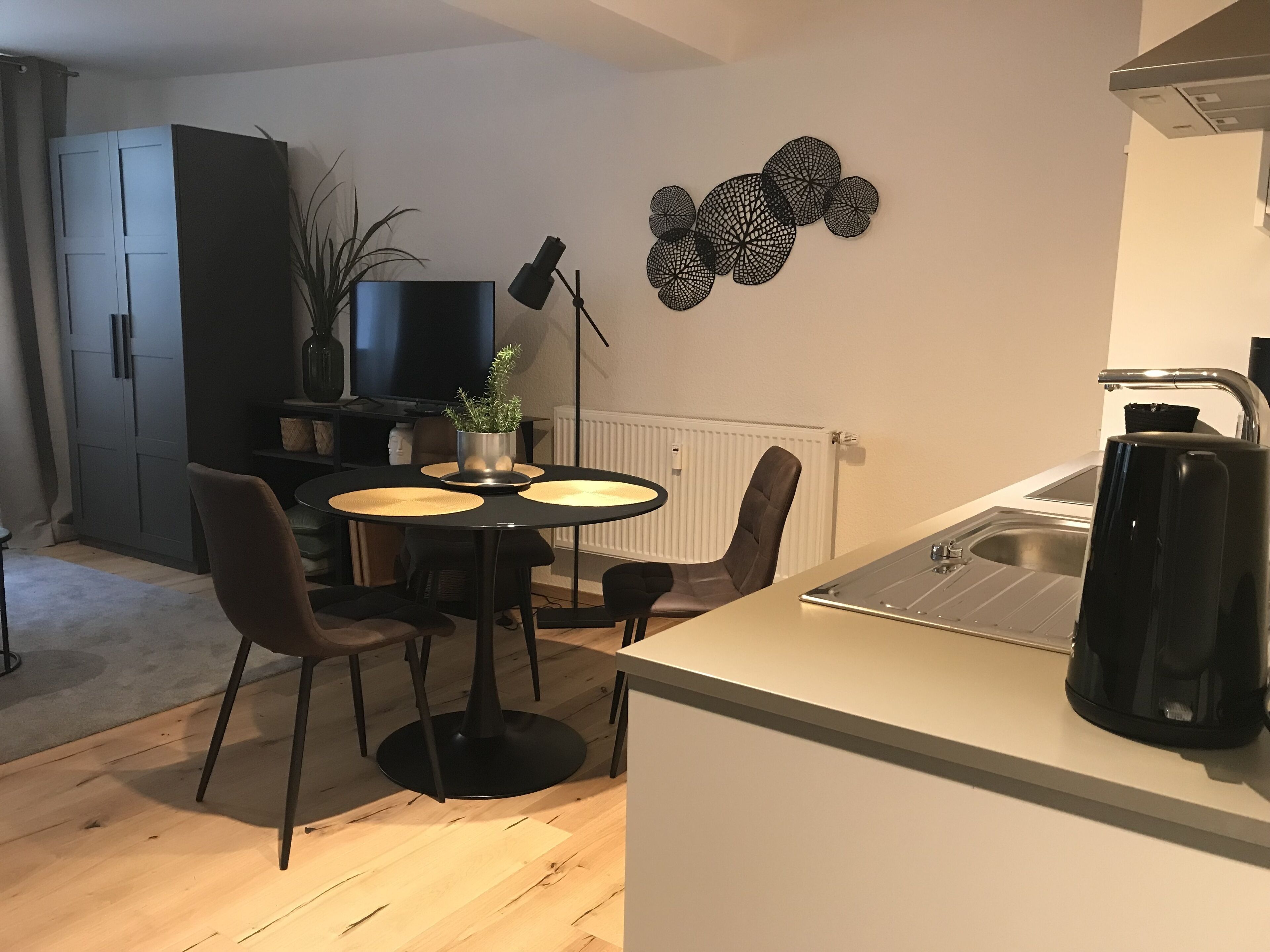 Cocina compacta con comedor, una cafetera negra y un adorno en la pared.