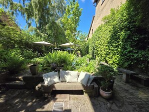 A courtyard with a stone bench, potted plants, and umbrellas. - Hotel Herrnschloesschen (Rothenburg ob der Tauber)