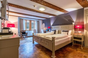 A bedroom with a large bed, a desk, a chair, and a window with curtains. - Hotel Herrnschloesschen (Rothenburg ob der Tauber)