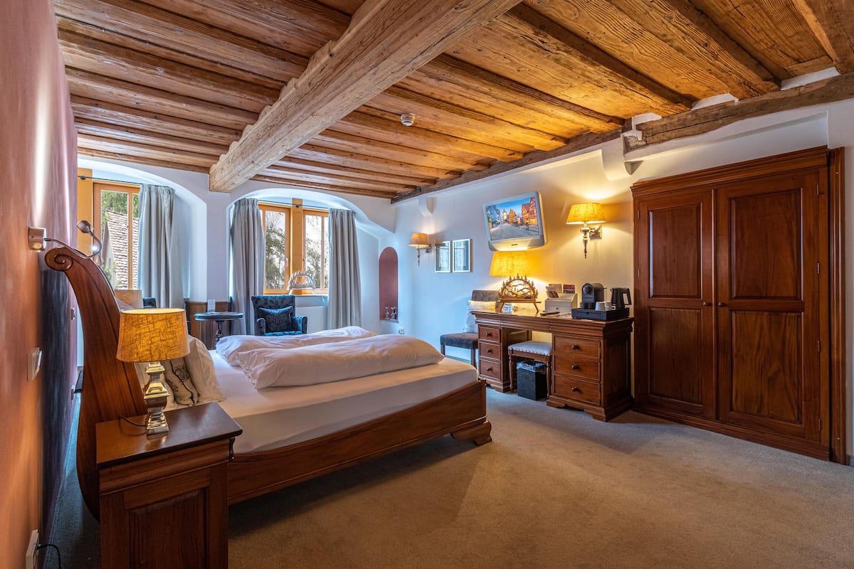 A bedroom with a wooden bed, a desk, a wardrobe, and a window with curtains.