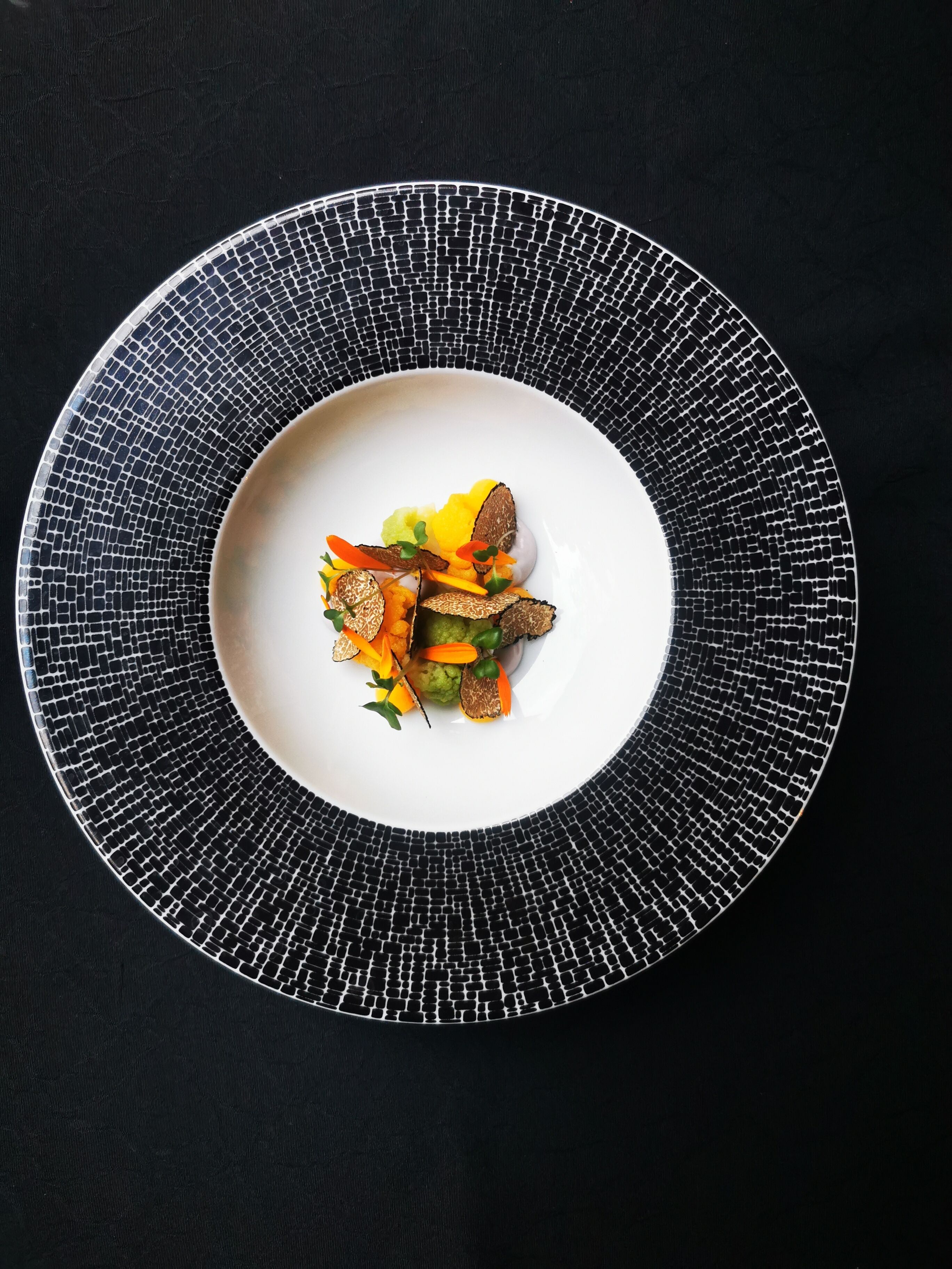 Un plato blanco con un diseño tipo mosaico, sobre una superficie negra.