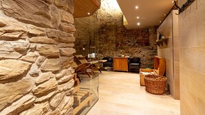 Interior de paredes de piedra con una mesa y sillas de madera, una cesta de mimbre y una chimenea de piedra.