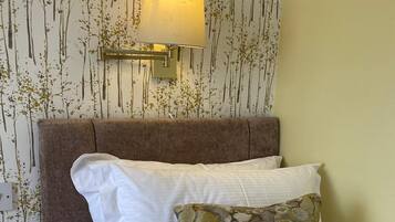A neatly made bed with white and patterned pillows, a brown headboard, and a wall-mounted lamp.
