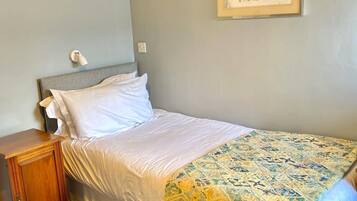 Un dormitorio con cama, mesita de noche, lámpara de pared y un cuadro floral enmarcado.