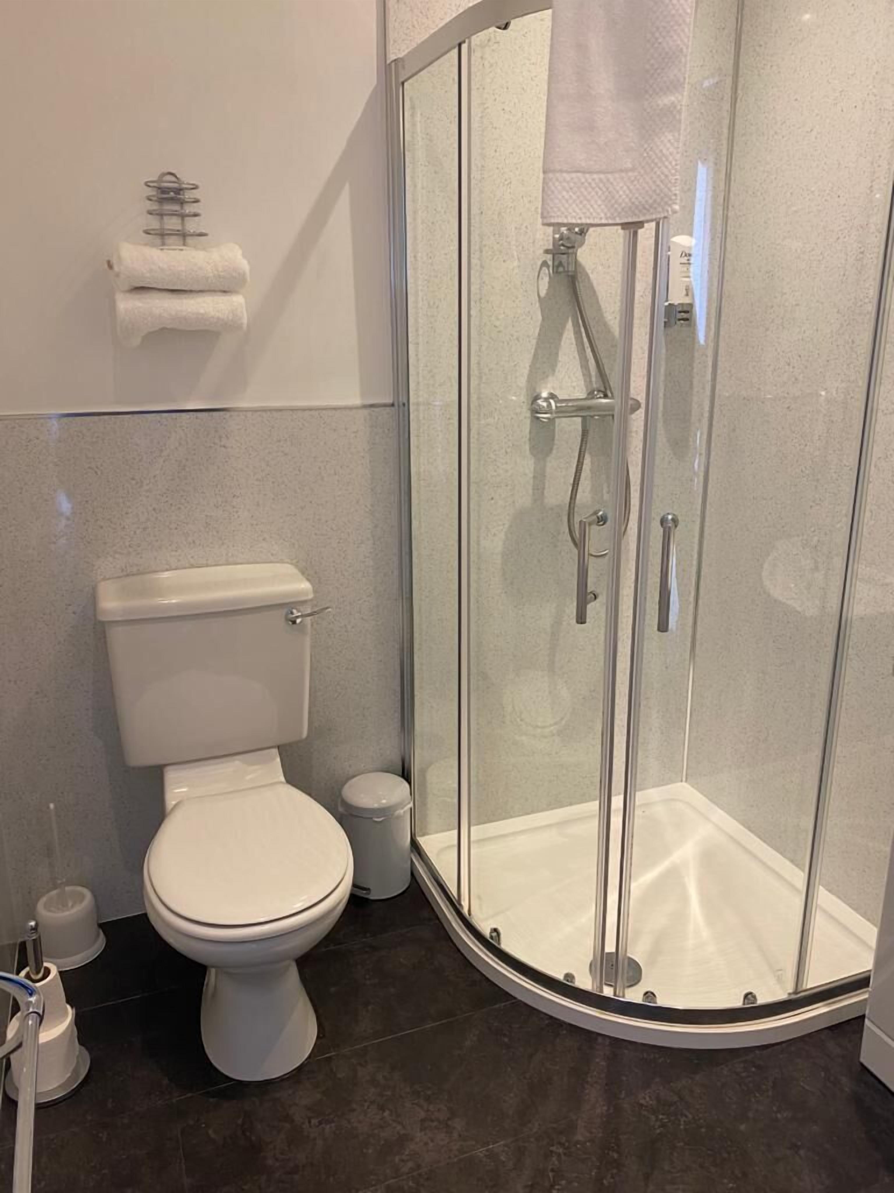 Ein modernes Badezimmer mit Toilette, einer gläsernen Duschkabine und einem Handtuchhalter.