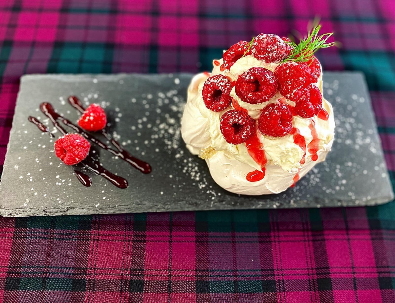 A dessert with raspberries and chocolate sauce on a slate board.
