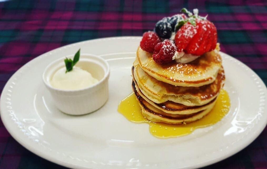 A stack of pancakes with berries and syrup on a white plate.