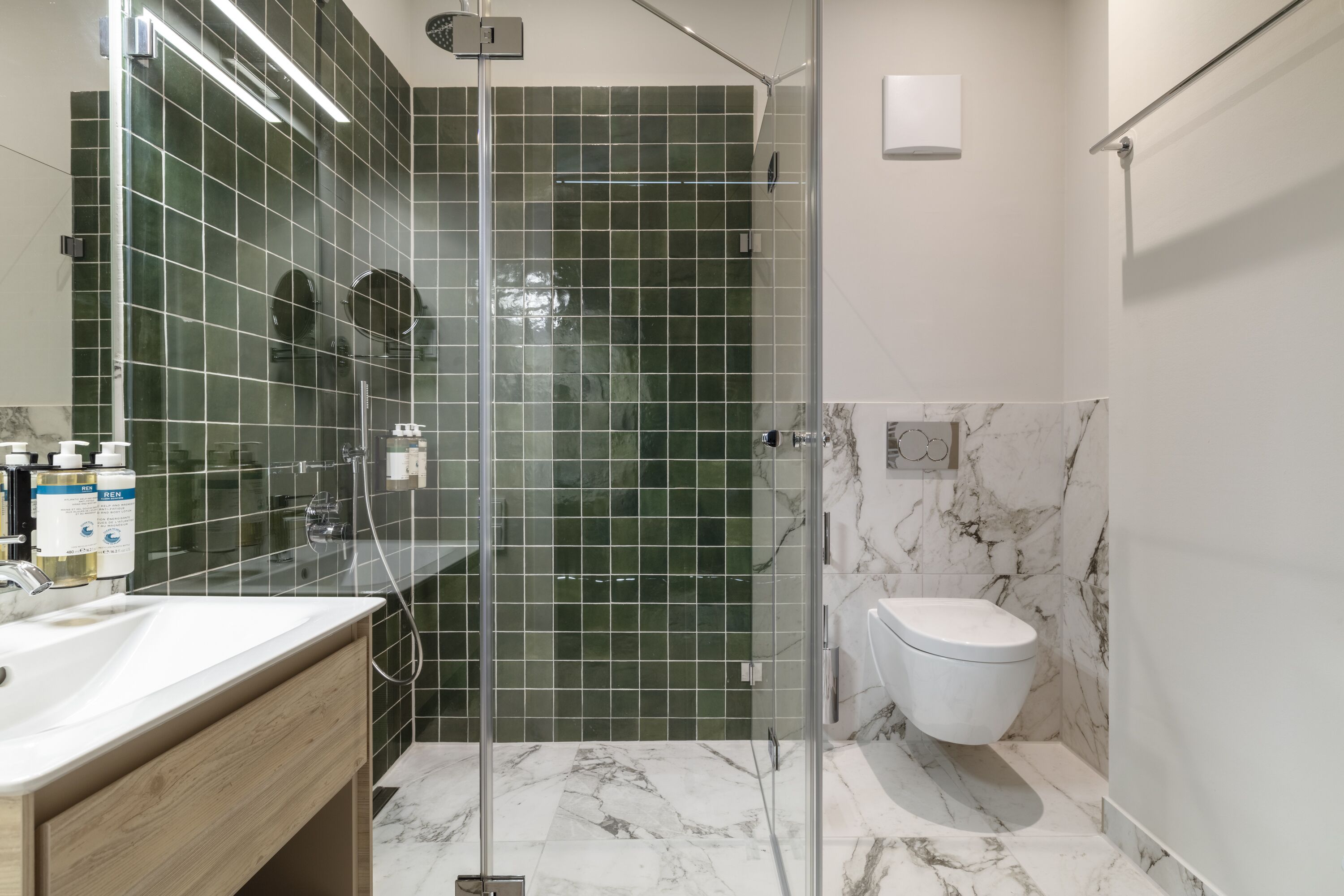 A modern bathroom with a glass-enclosed shower, a white sink, and a marble-tiled floor.